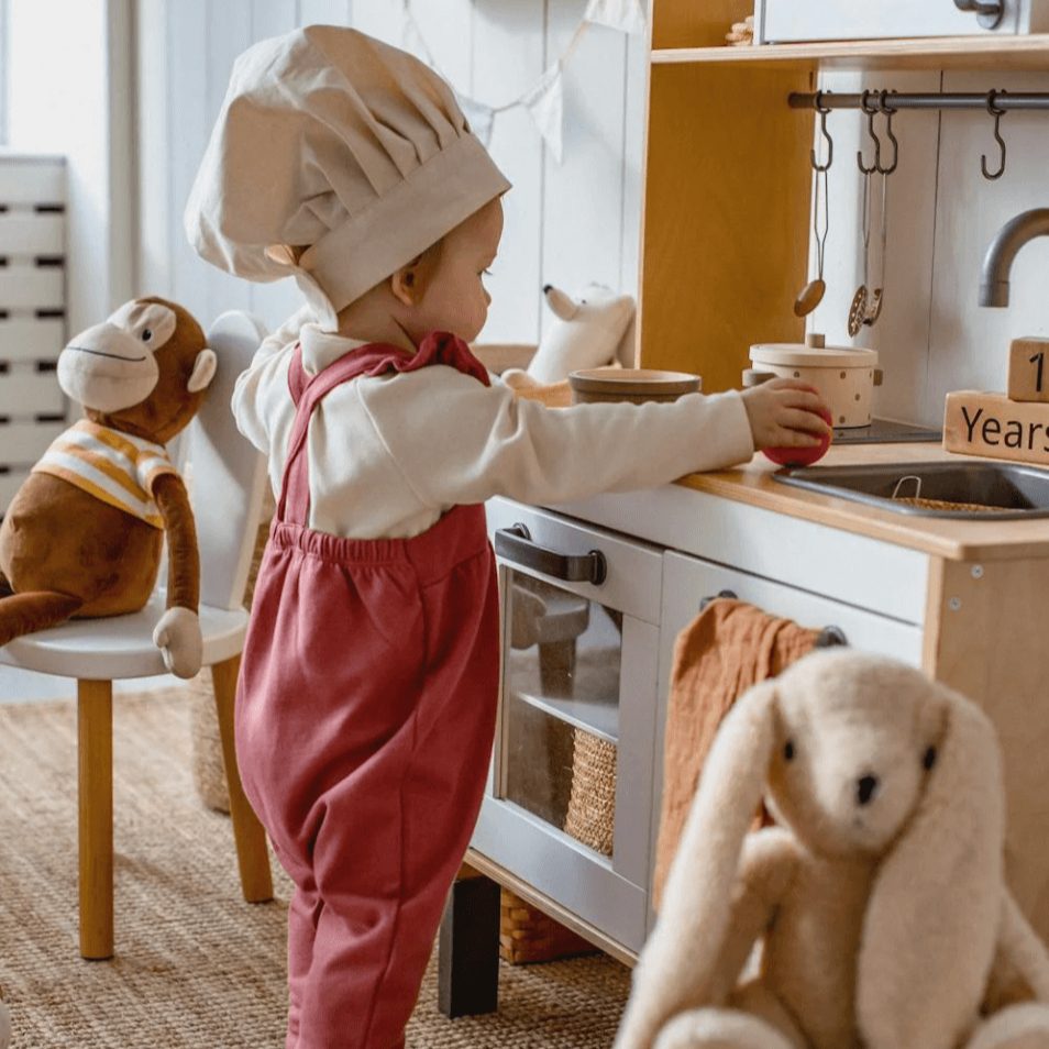 Child dressed as a chef playing with a kitchen set